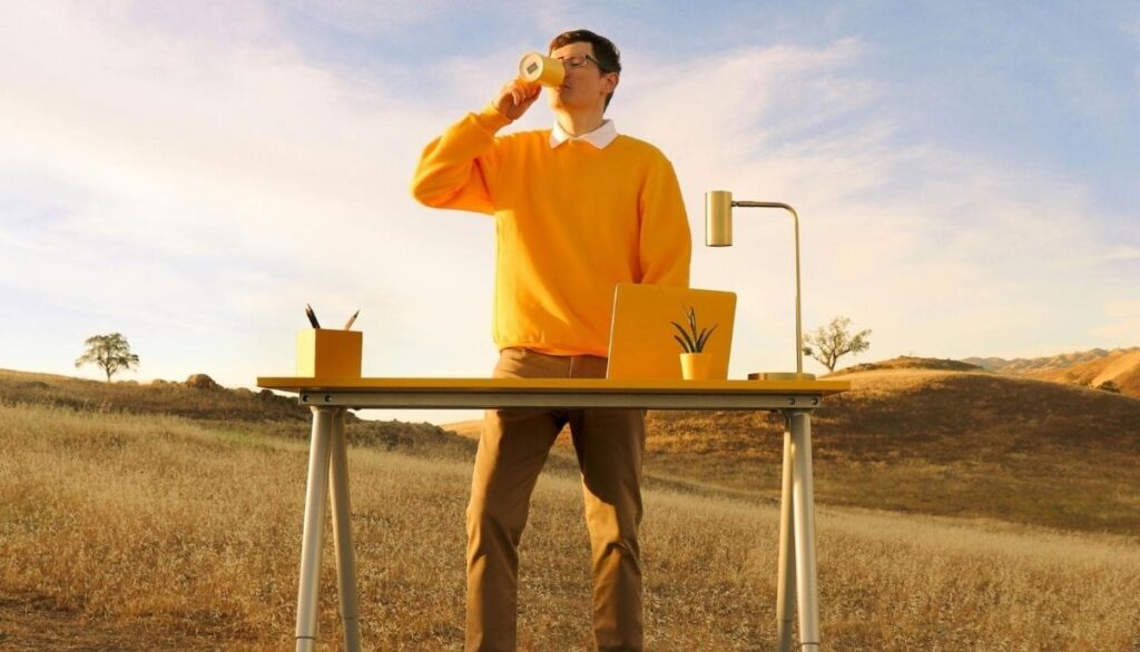 Man drinking coffee in front of his computer on an open landscape.